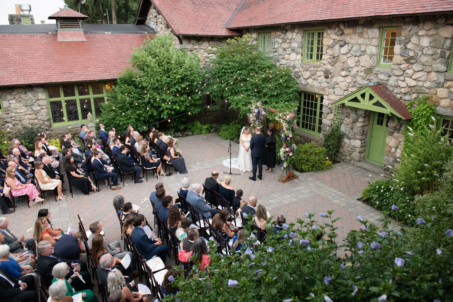 Wedding guests seated outdoors at a rustic stone venue during a ceremony.