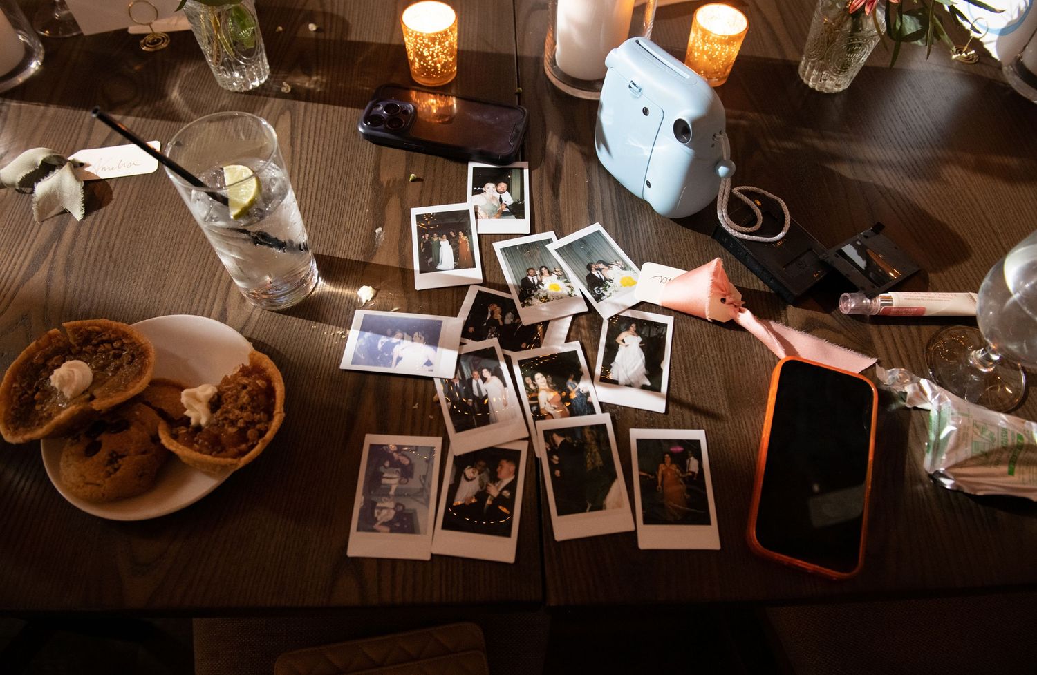 Candlelit table with scattered polaroid photos and drinks creating an intimate nostalgic atmosphere.