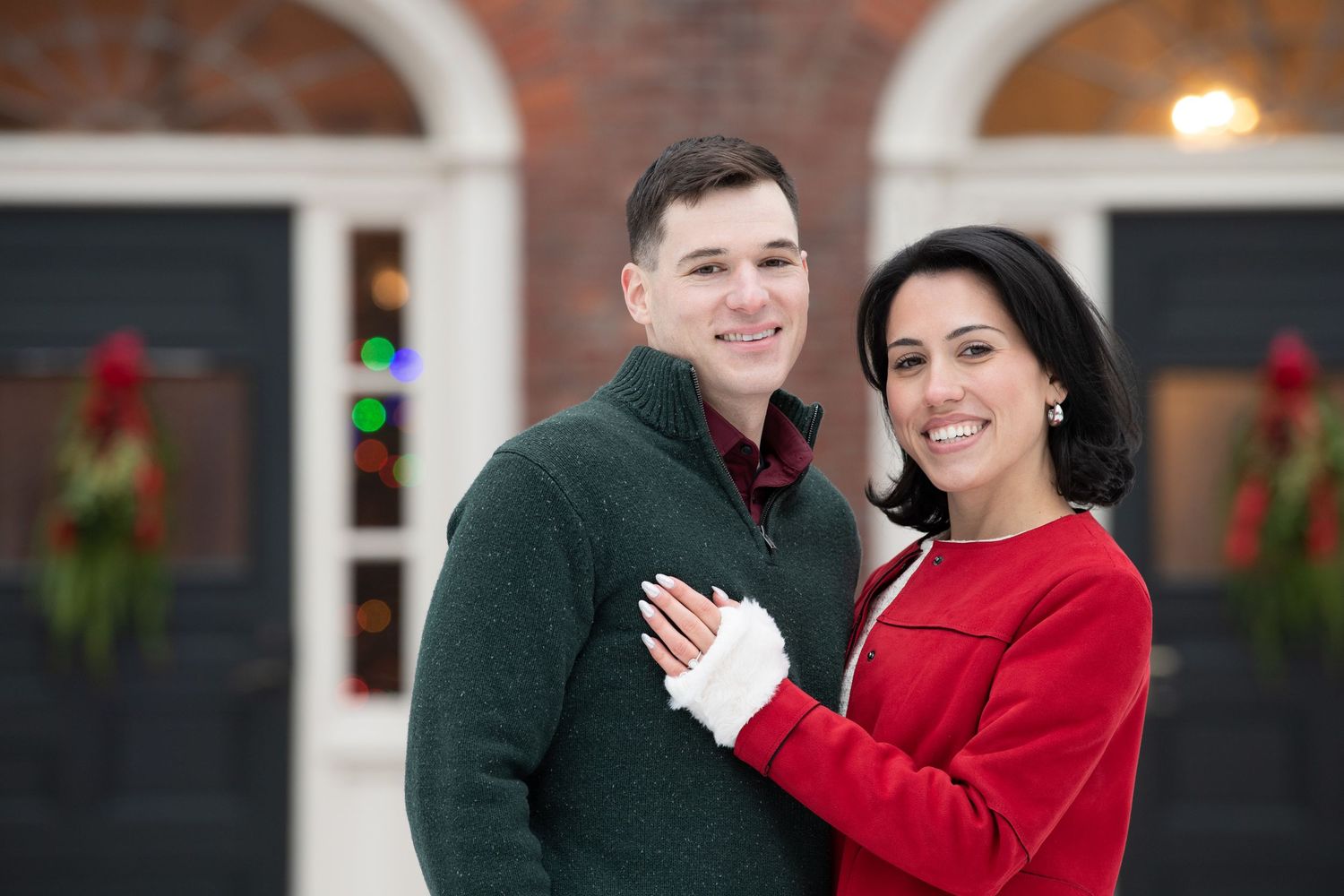 A couple in red and dark green sweaters poses together outdoors during a winter photo session.