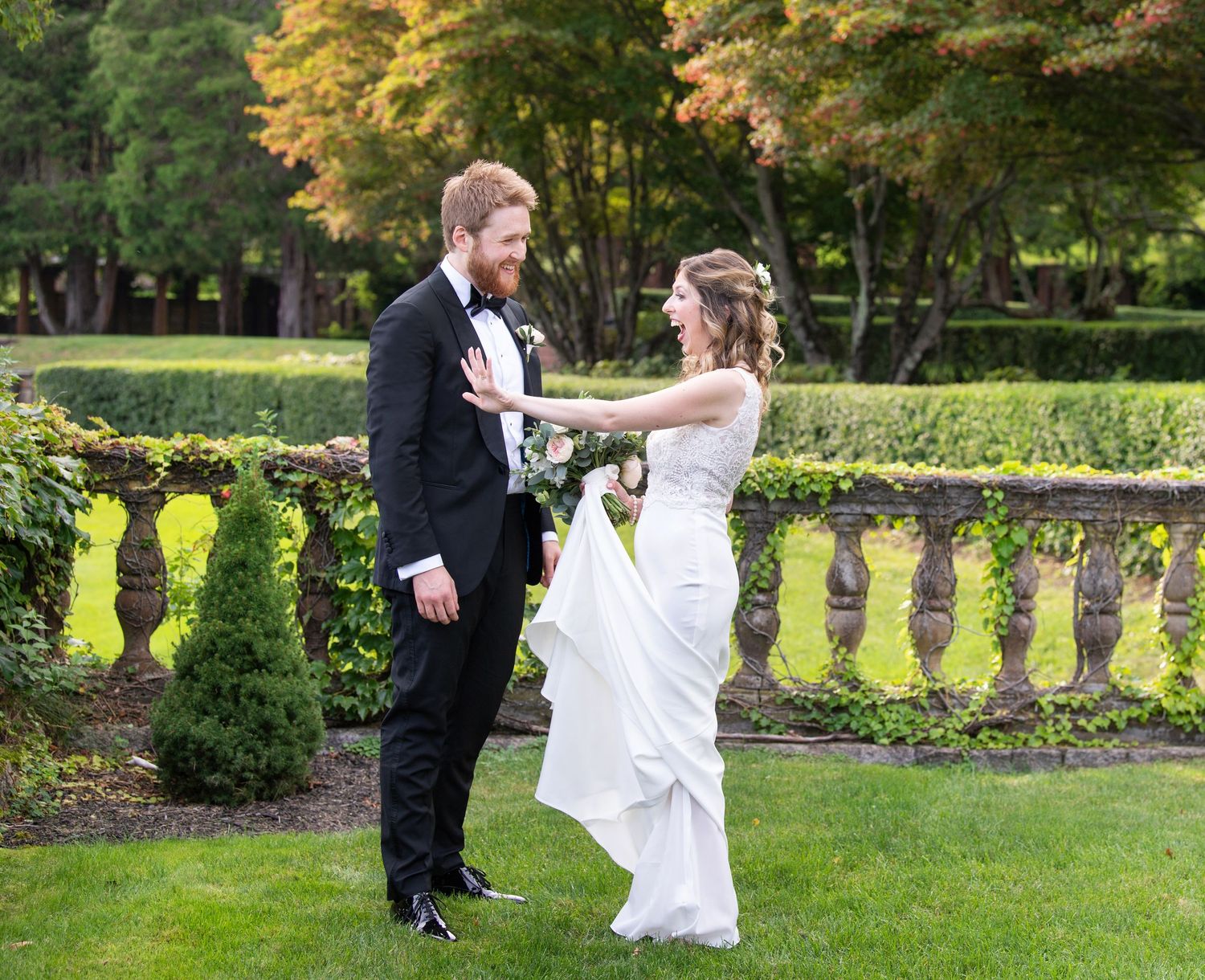A joyful couple shares playful moments in a lush garden setting with ornate stone balusters and autumn foliage.