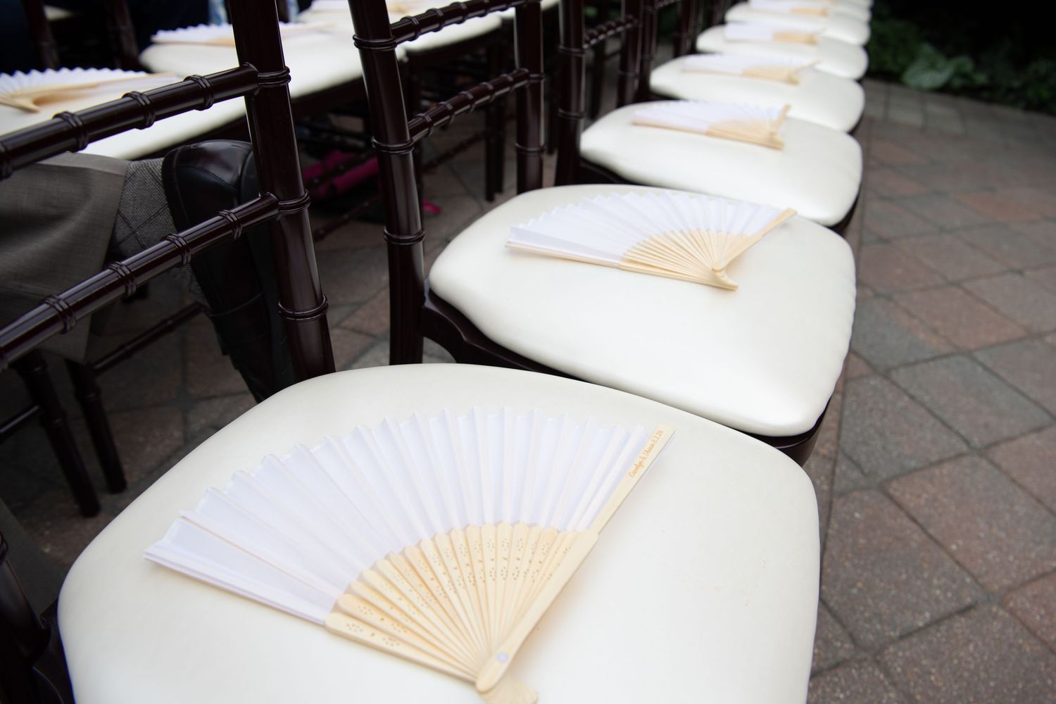 White paper fans arranged in a row on ceremony chairs create an elegant wedding ceremony setting.