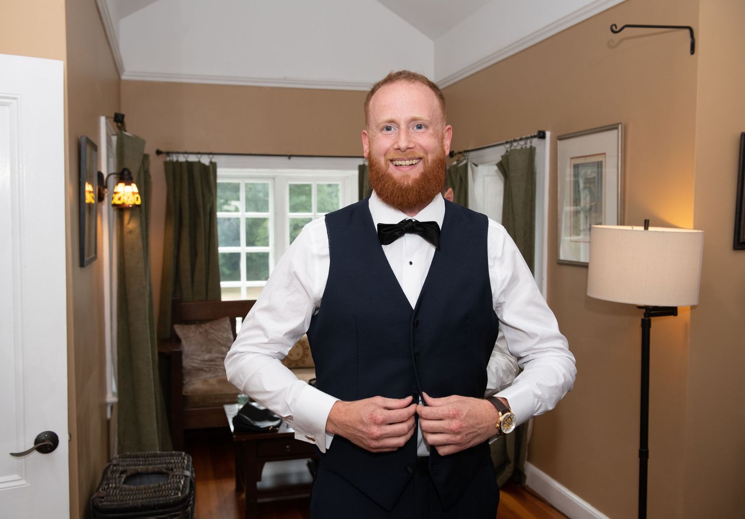 Groom adjusts his vest while getting ready in formal attire with bow tie.