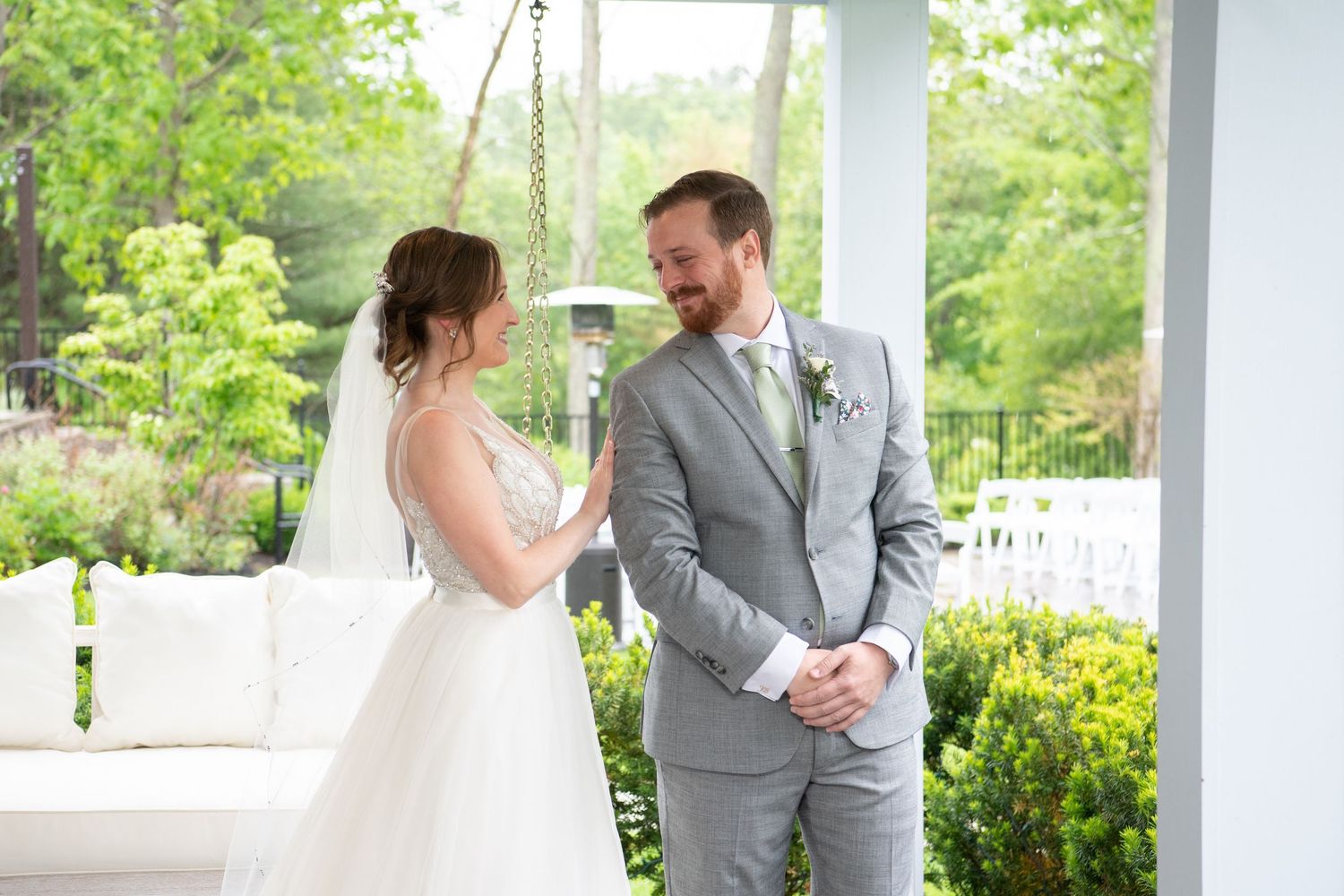 Wedding couple shares a romantic moment on a white porch with green foliage in the background.