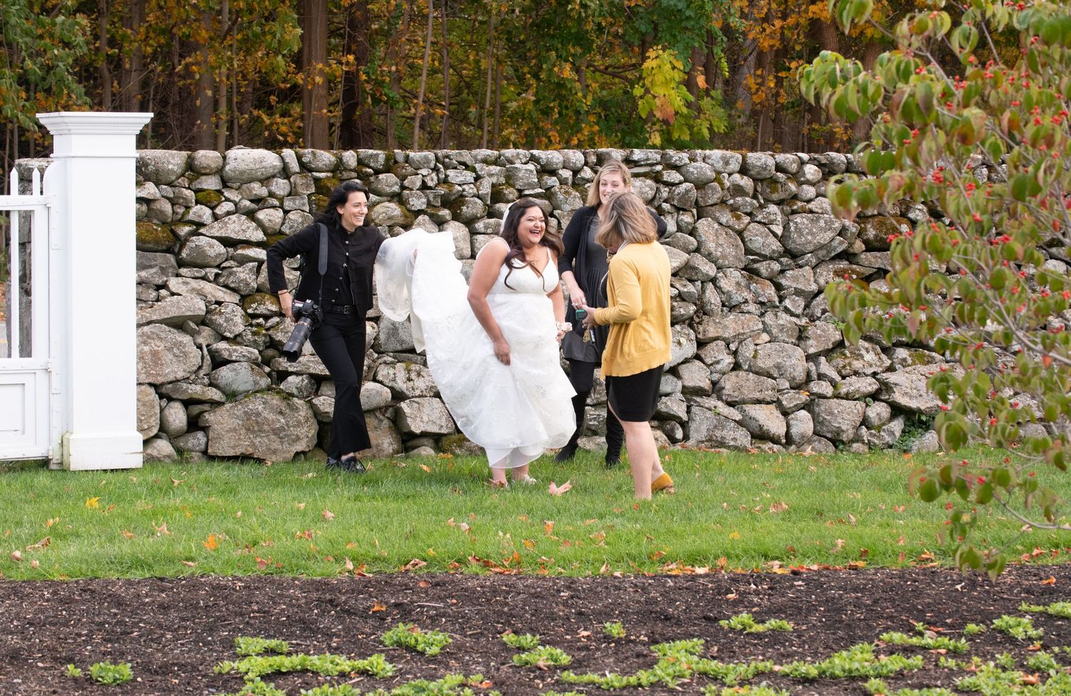 Wedding party running along stone wall during fall season outdoor celebration.