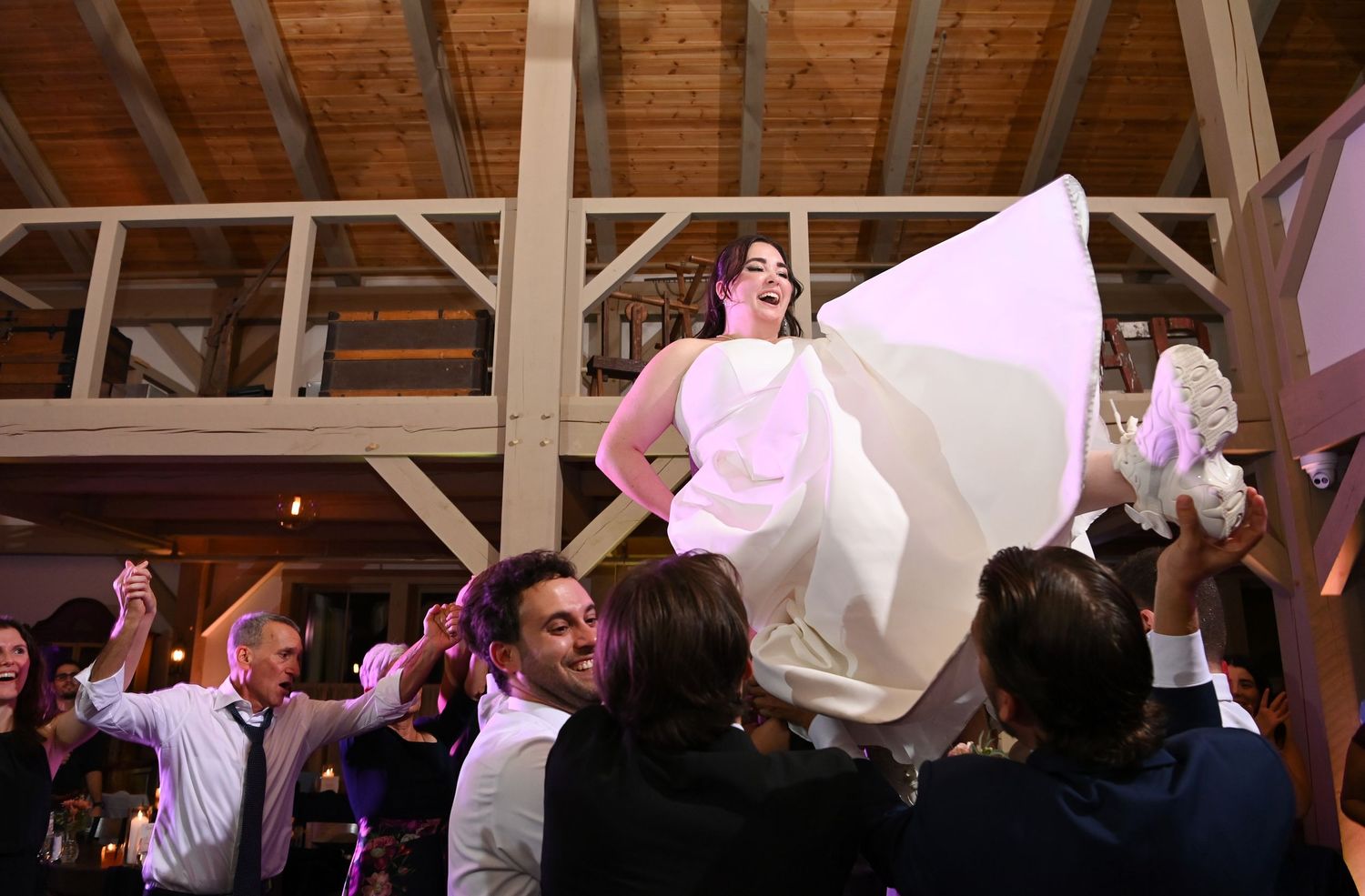 Wedding reception guests wave white napkins in celebration during a festive dance party in a rustic wooden venue.