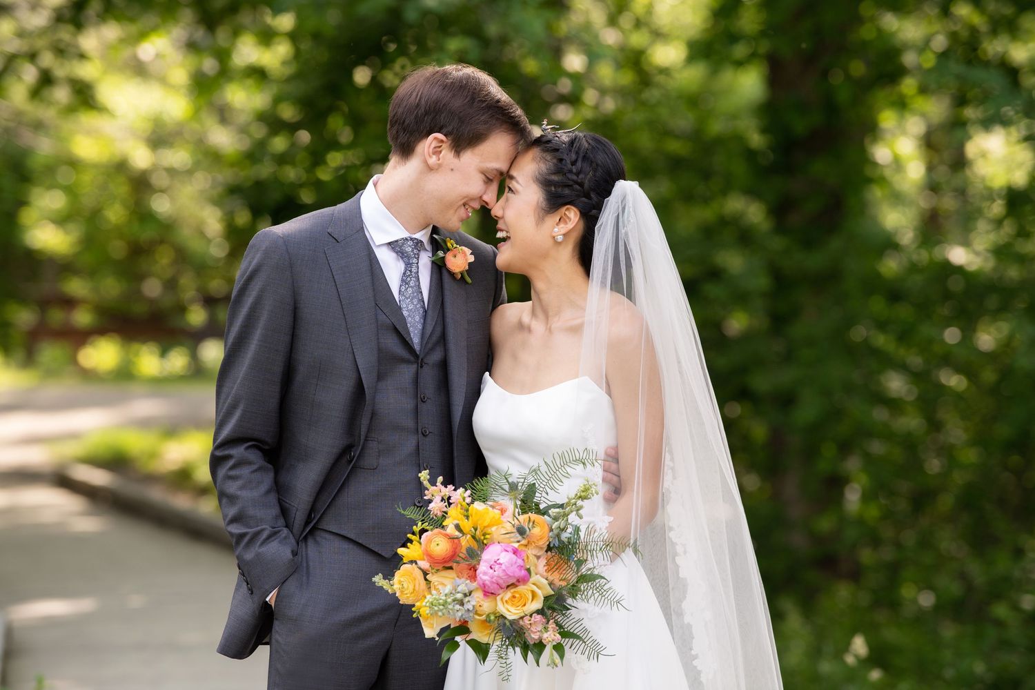A couple shares a romantic moment in a park while wearing traditional wedding attire with vibrant flowers.