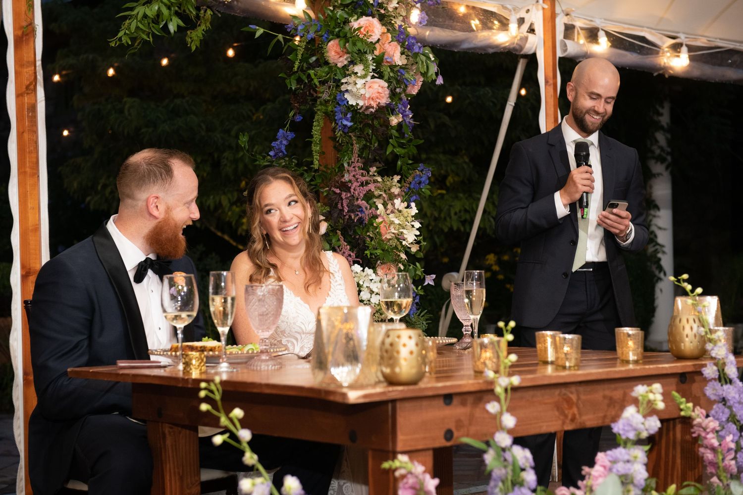 Wedding celebration at outdoor venue with suspended floral decorations and wooden dining tables.