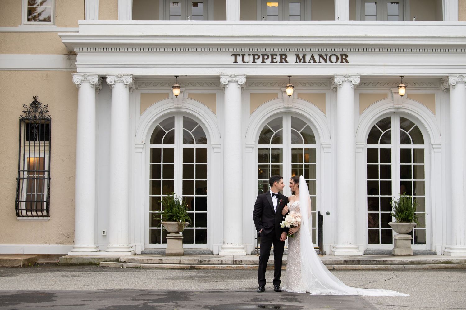 Bride and groom pose in front of Tupper Manor elegant white colonial wedding venue.