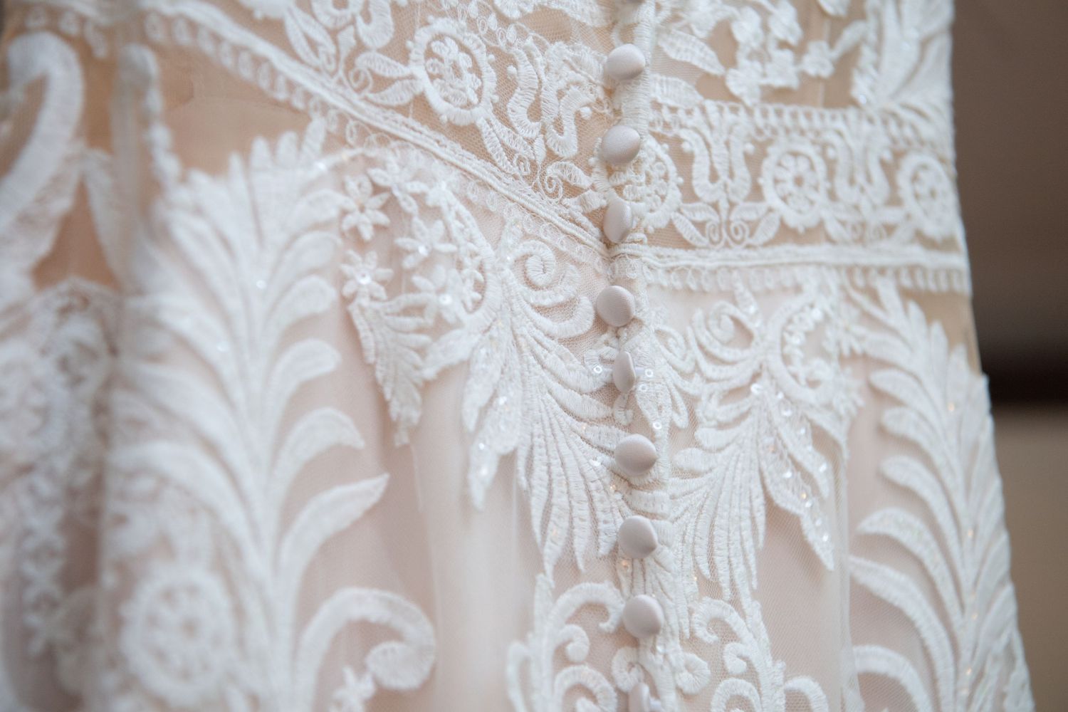 Delicate lace detailing on a white wedding dress shows intricate floral patterns and textures.
