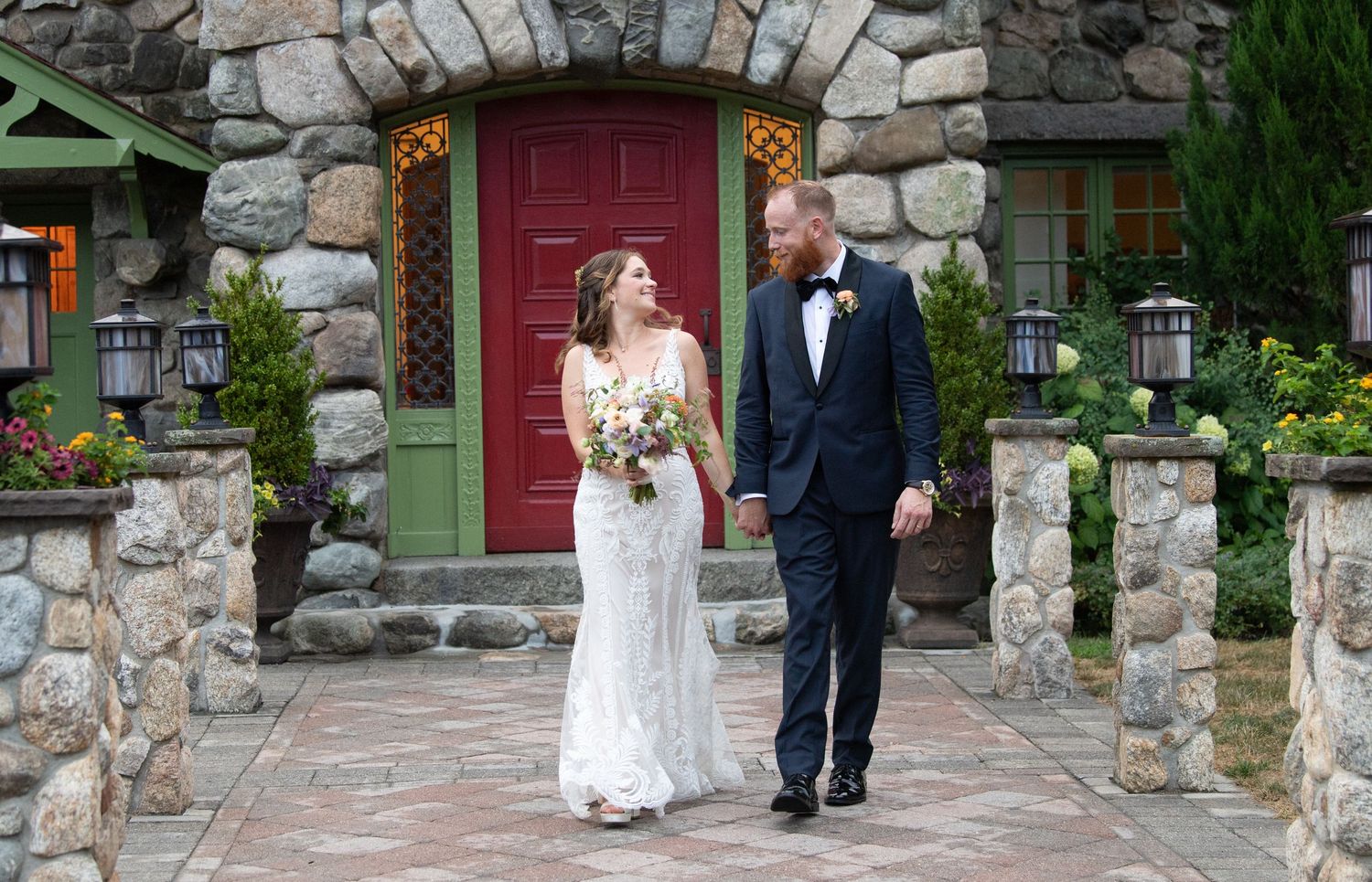 Wedding party walks along stone pathway near red door entrance.