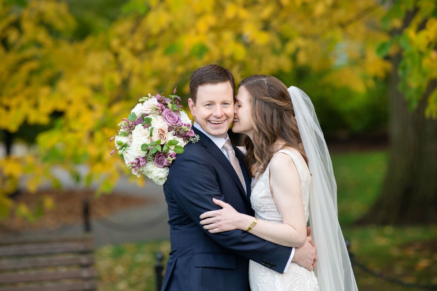 A romantic wedding couple shares a joyful moment together in a lush garden with autumn foliage in the background.