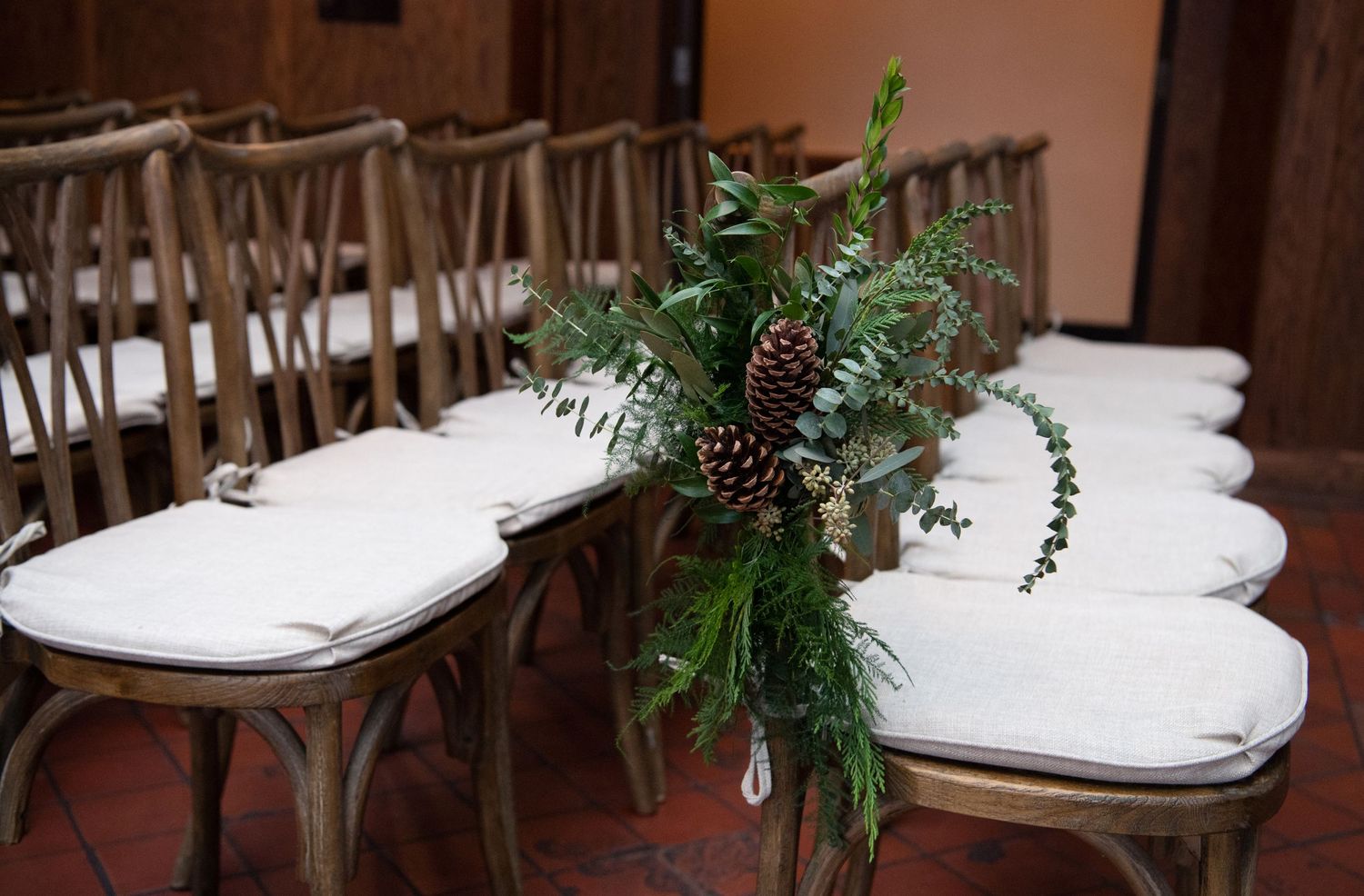 White folding chairs with plush cushions arranged in rows for an indoor ceremony with greenery accents.