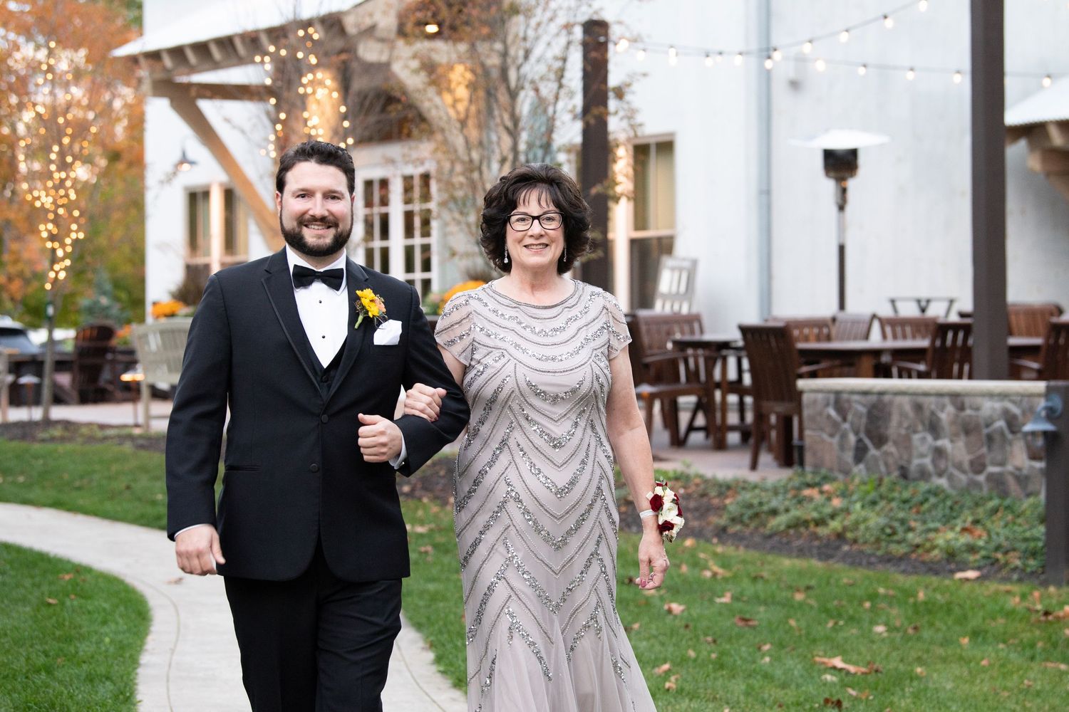 Two people in formal attire walk together on a path outside a venue during a special celebration.