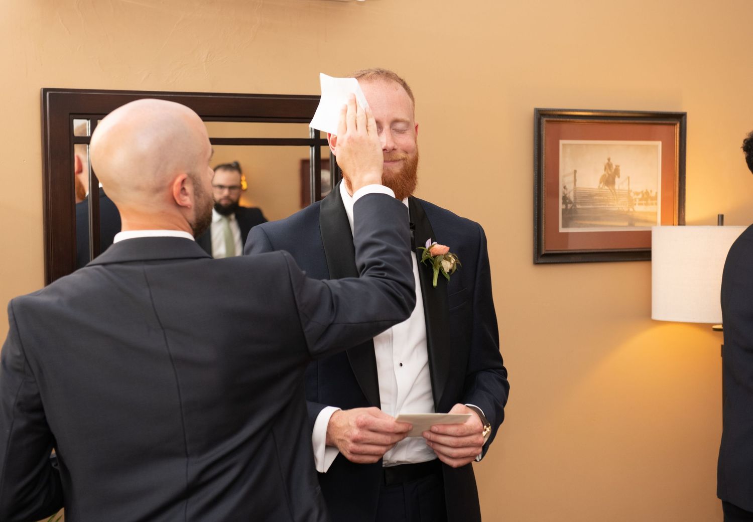 A groom getting his tie adjusted while holding papers before the wedding ceremony.