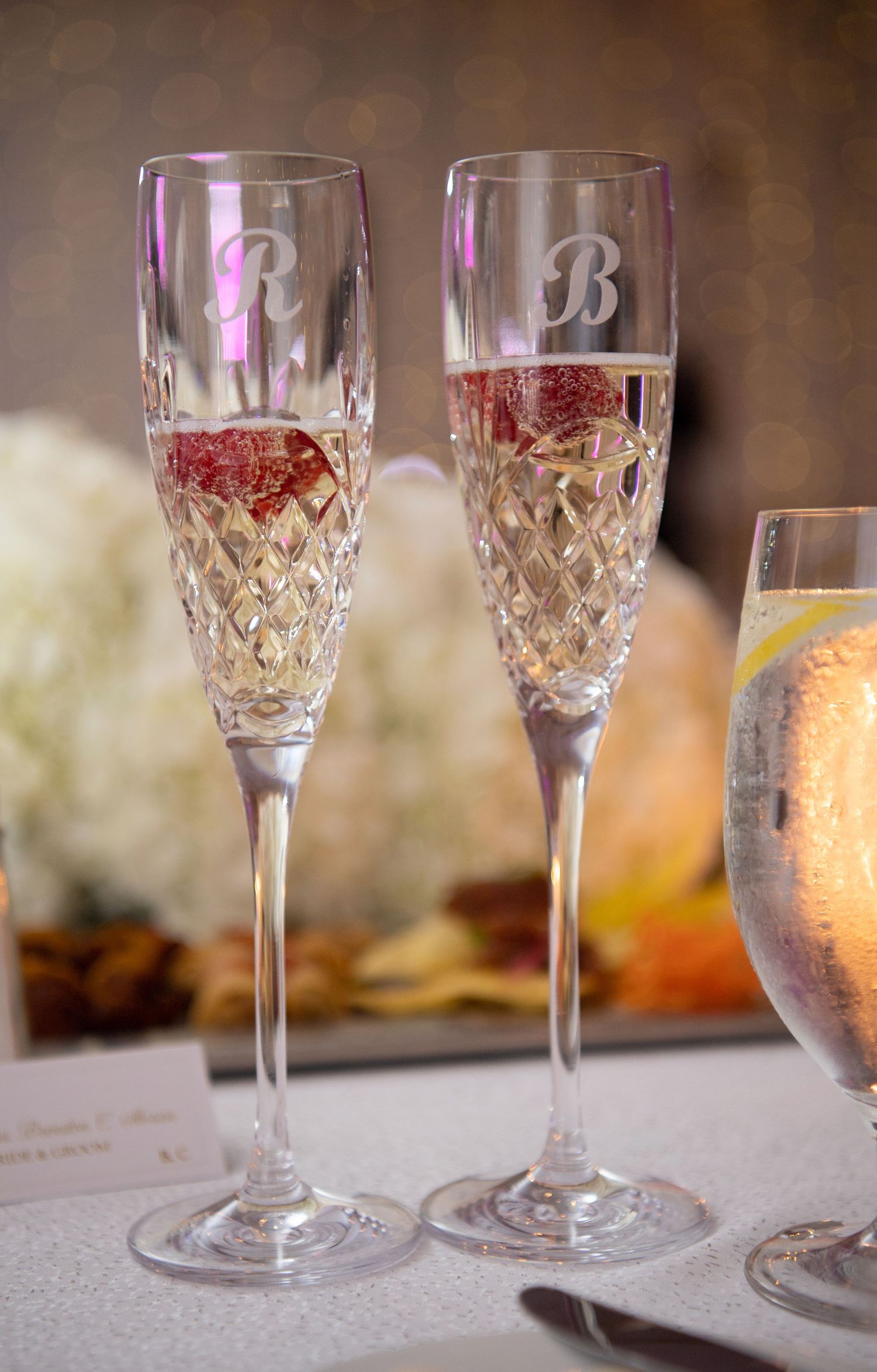 Two elegant crystal wine glasses with cut diamond patterns sit side by side on a white tablecloth in soft lighting.