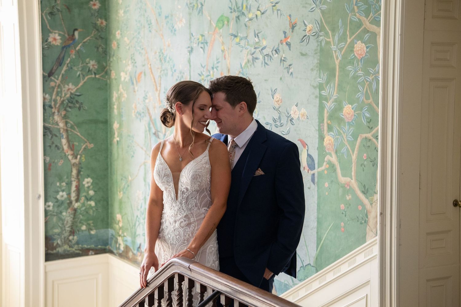 Two newlyweds stand intimately close in a room with elegant mint-green floral wallpaper for formal wedding portraits. Long Hill Wedding