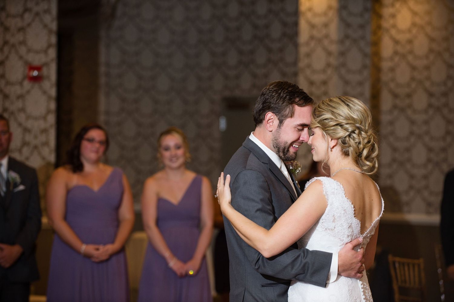 Romantic moment between newlyweds with bridesmaids in purple dresses watching in the background.