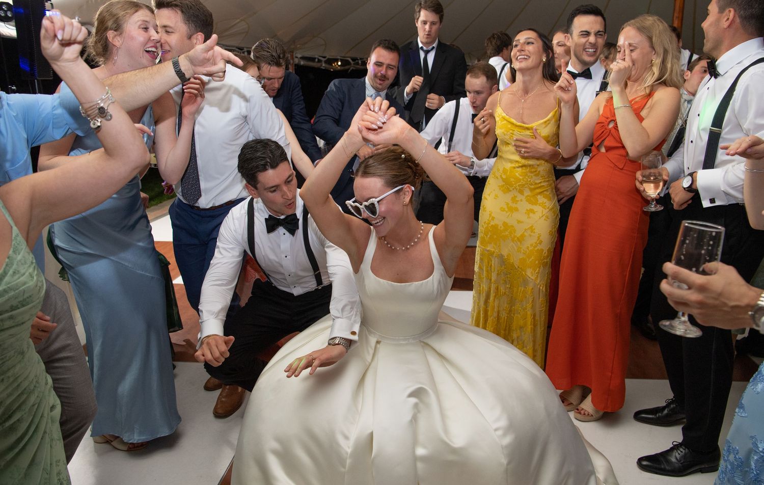 Bride in white gown dancing joyfully with guests at a lively wedding reception celebration.