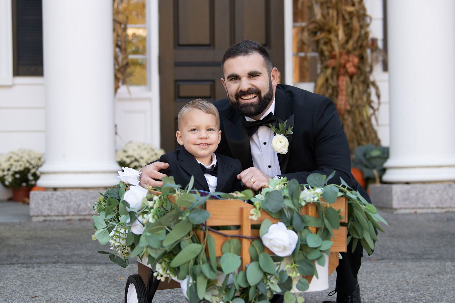 A formal wedding photo with greenery and white floral garland decorations in front of white columns.
