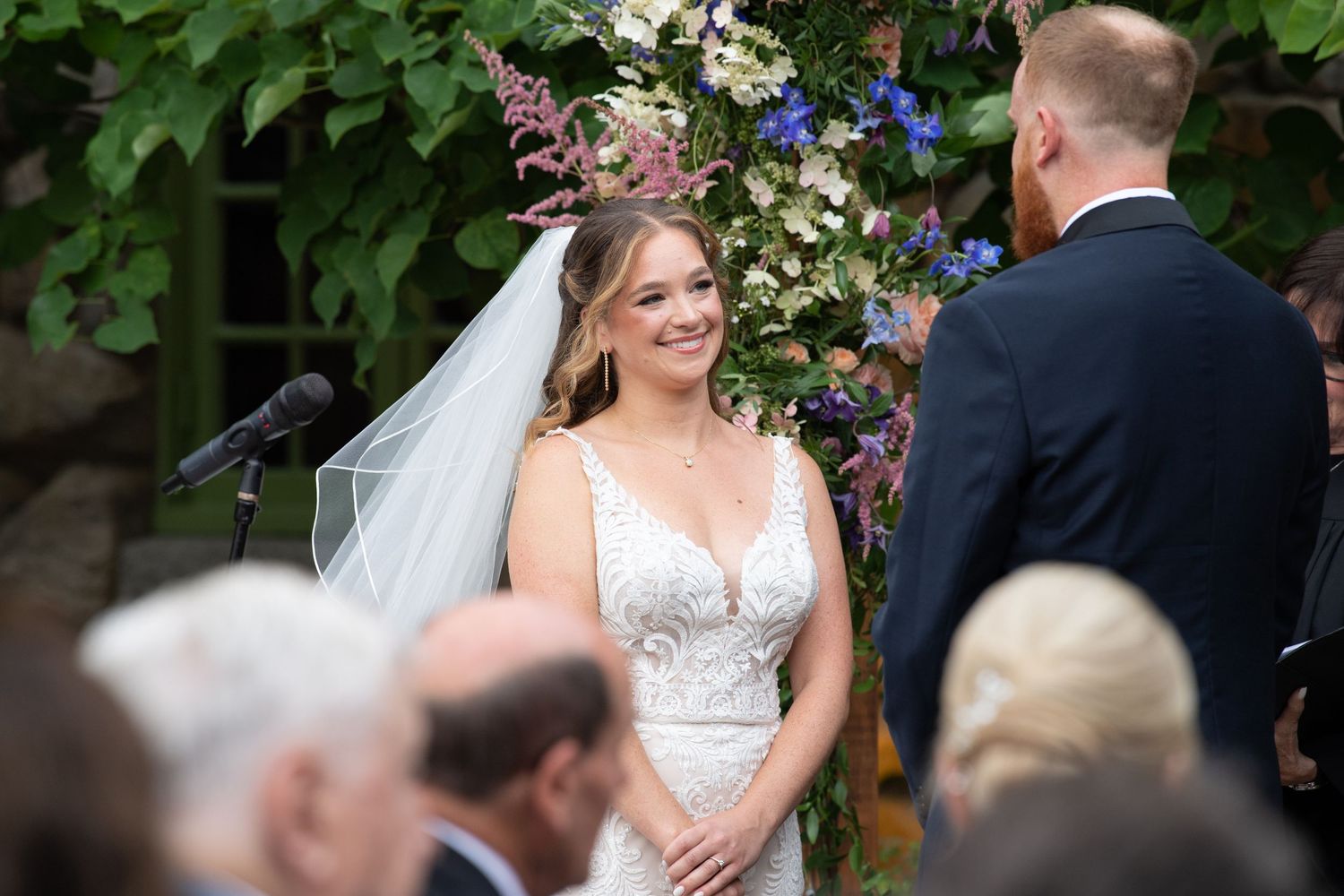 Outdoor wedding ceremony with floral arch and couple exchanging vows.