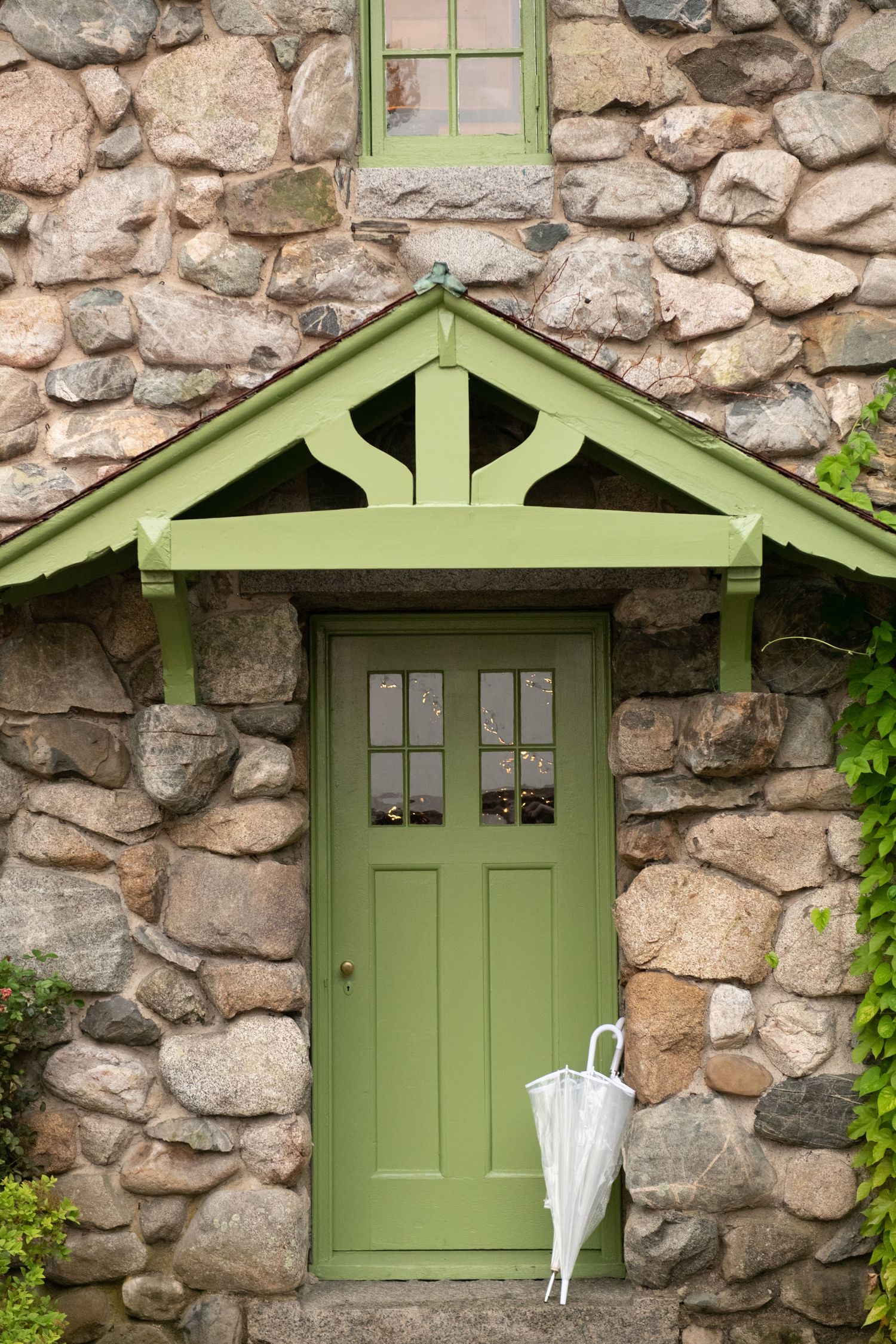 Green wooden doors set against rustic stone wall with white umbrella leaning beside them.