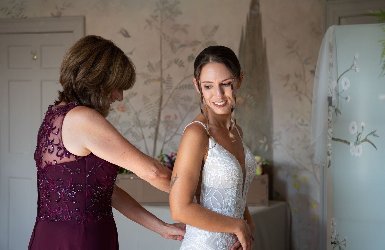 Elegant wedding preparation scene with bridesmaids in purple dresses helping with final touches in a vintage room.