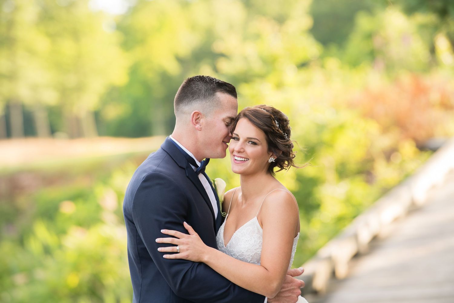 A romantic wedding couple embraces in a sunlit garden setting during their outdoor portrait session.