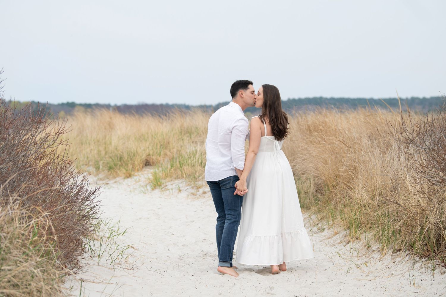 A loving couple shares an intimate moment while walking together on a sandy beach path in natural surroundings.