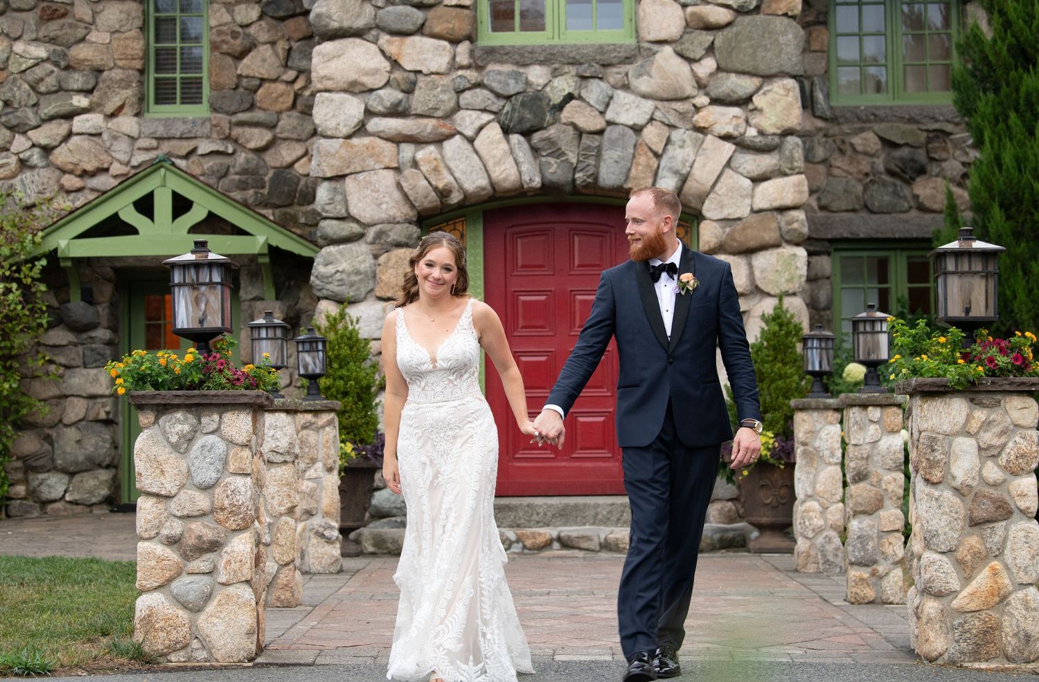 Newlyweds celebrate outside a charming stone cottage with green trim and red door.
