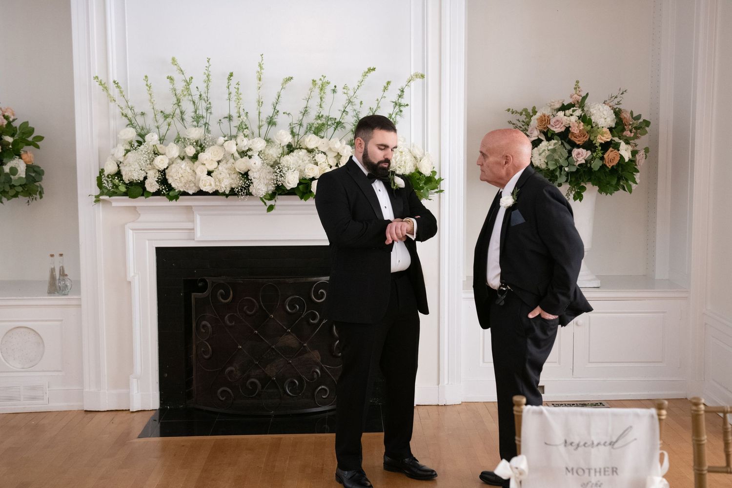 Elegant wedding ceremony scene with white floral arrangements and guests in formal attire in a bright interior space.