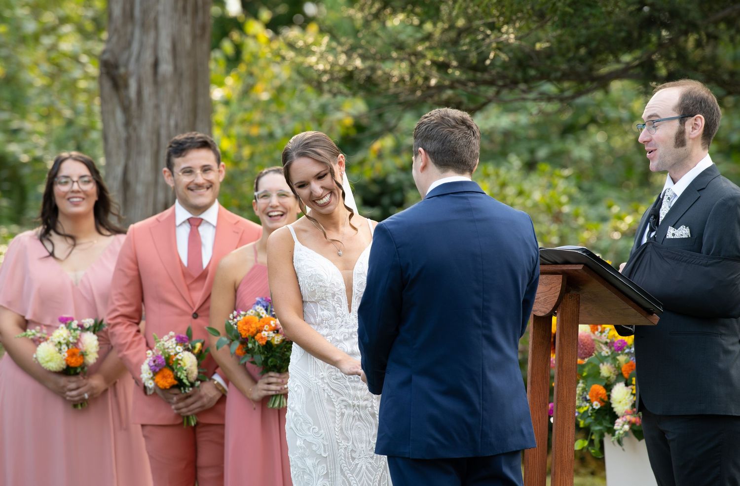 Outdoor wedding ceremony with autumn floral arrangements and guests gathered in a wooded garden setting.