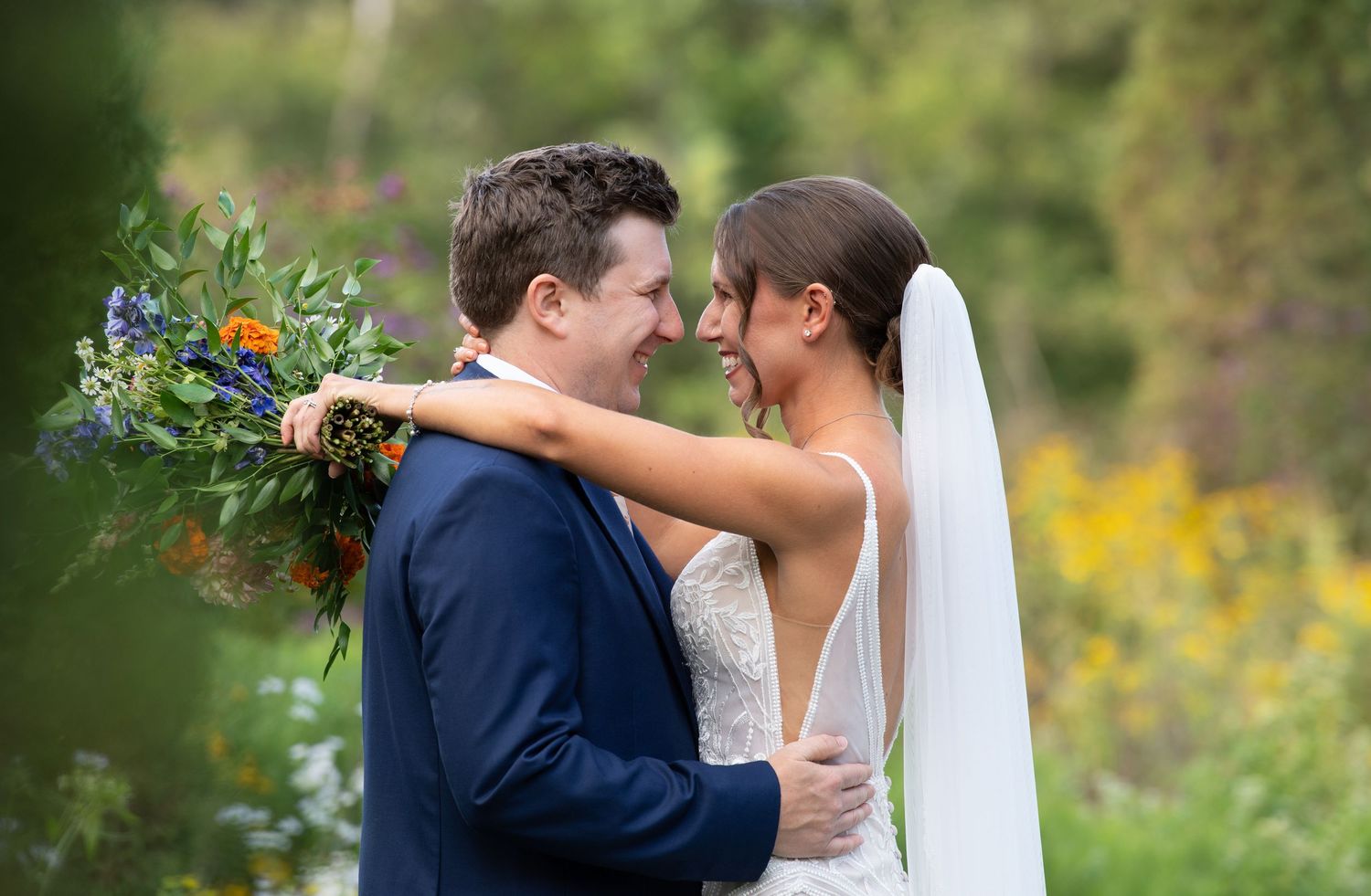 A romantic couple shares intimate moments in a garden setting with yellow wildflowers and greenery in the background.