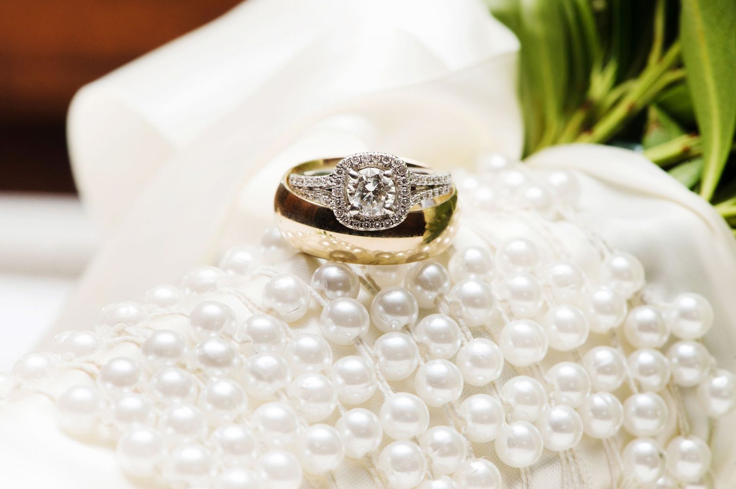 White pearls and diamond rings displayed on shiny reflective surface for luxury wedding jewelry photography.