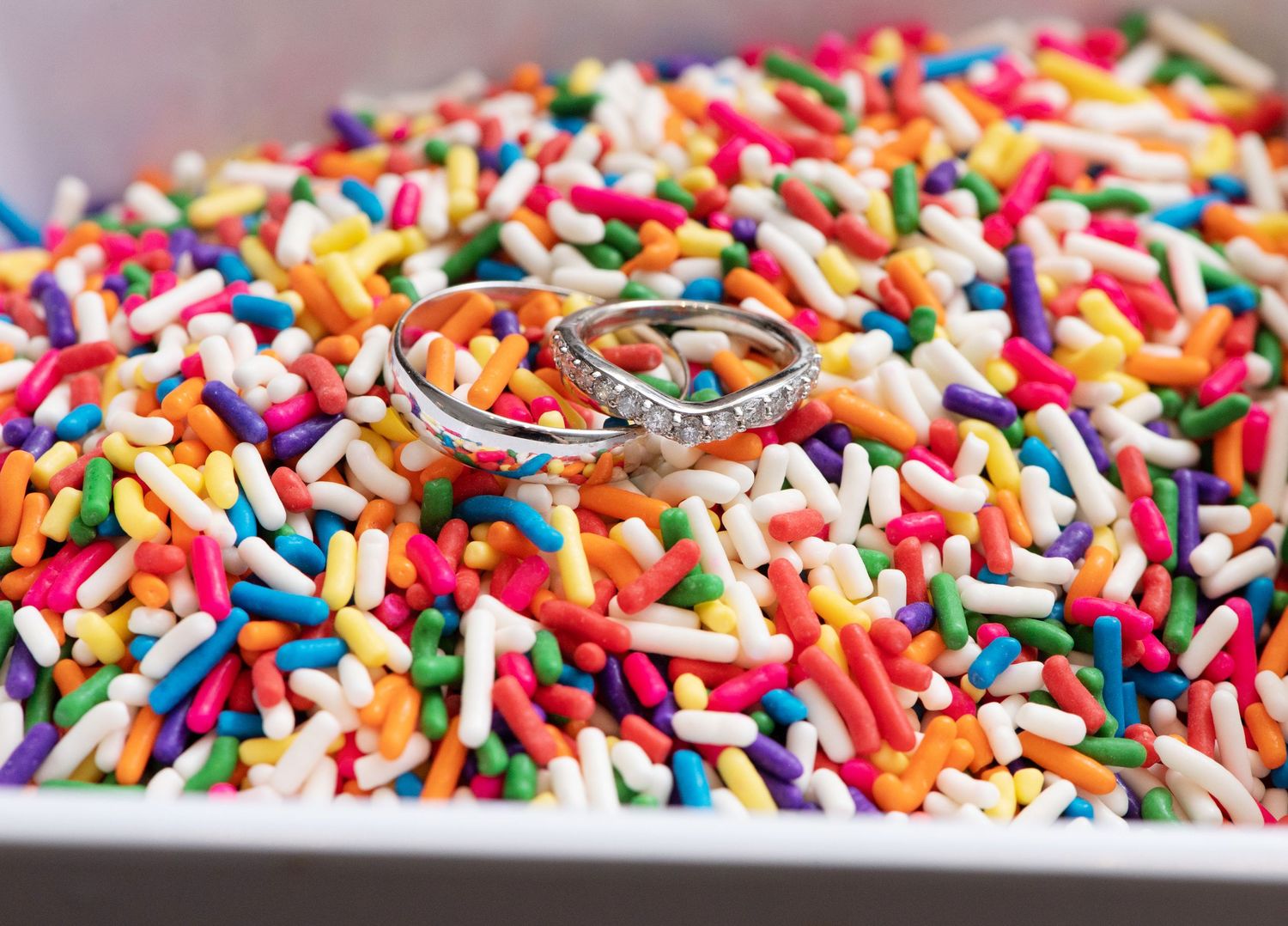 Wedding rings nestled in colorful rainbow sprinkles on a silver tray create a festive and romantic display.