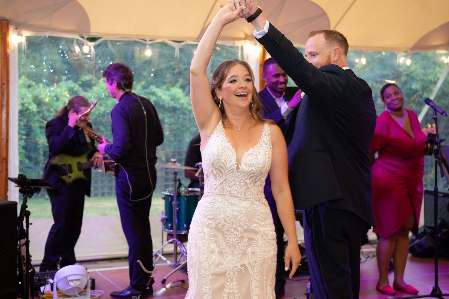 Wedding celebration in a tent with guests dancing under purple lighting.