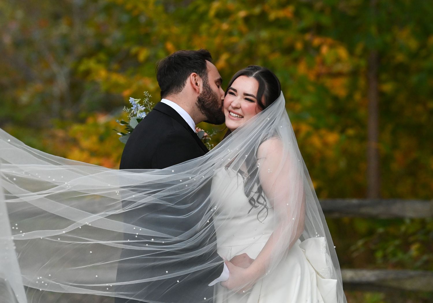 Bride and groom share an intimate moment as her long veil flows in the autumn breeze.