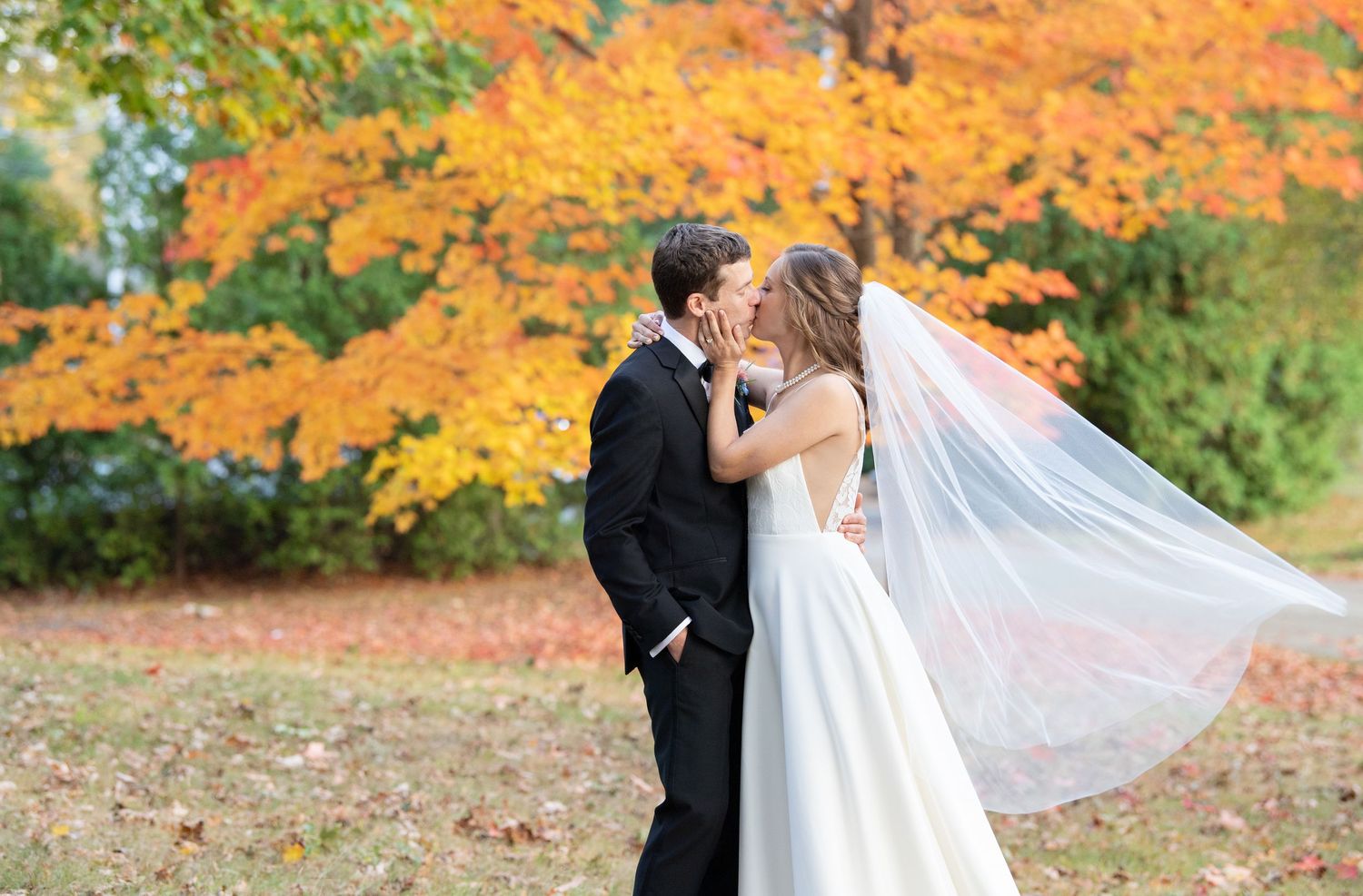 A romantic wedding couple embraces in a stunning autumn setting with vibrant orange and yellow fall foliage.
