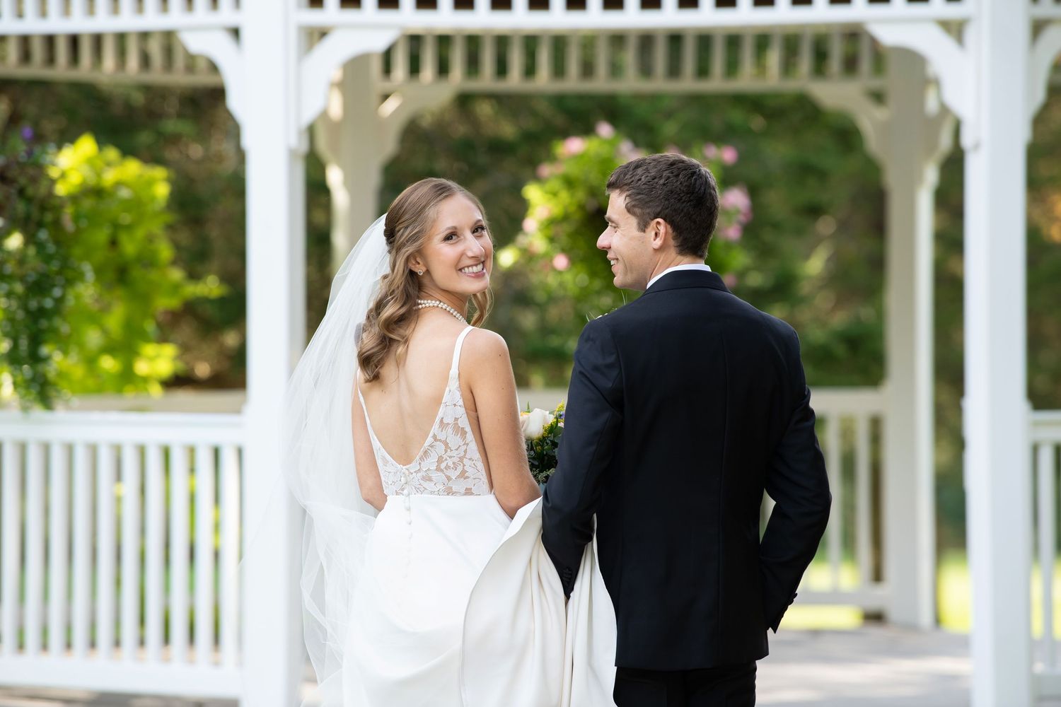 A romantic wedding photo series with a couple in formal attire posing by a white gazebo in a garden setting.