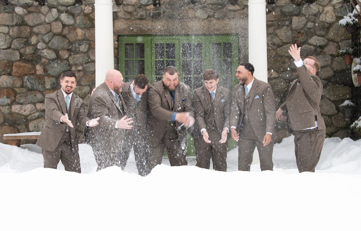 A group in matching gray suits playfully throws snow at each other during a winter celebration.