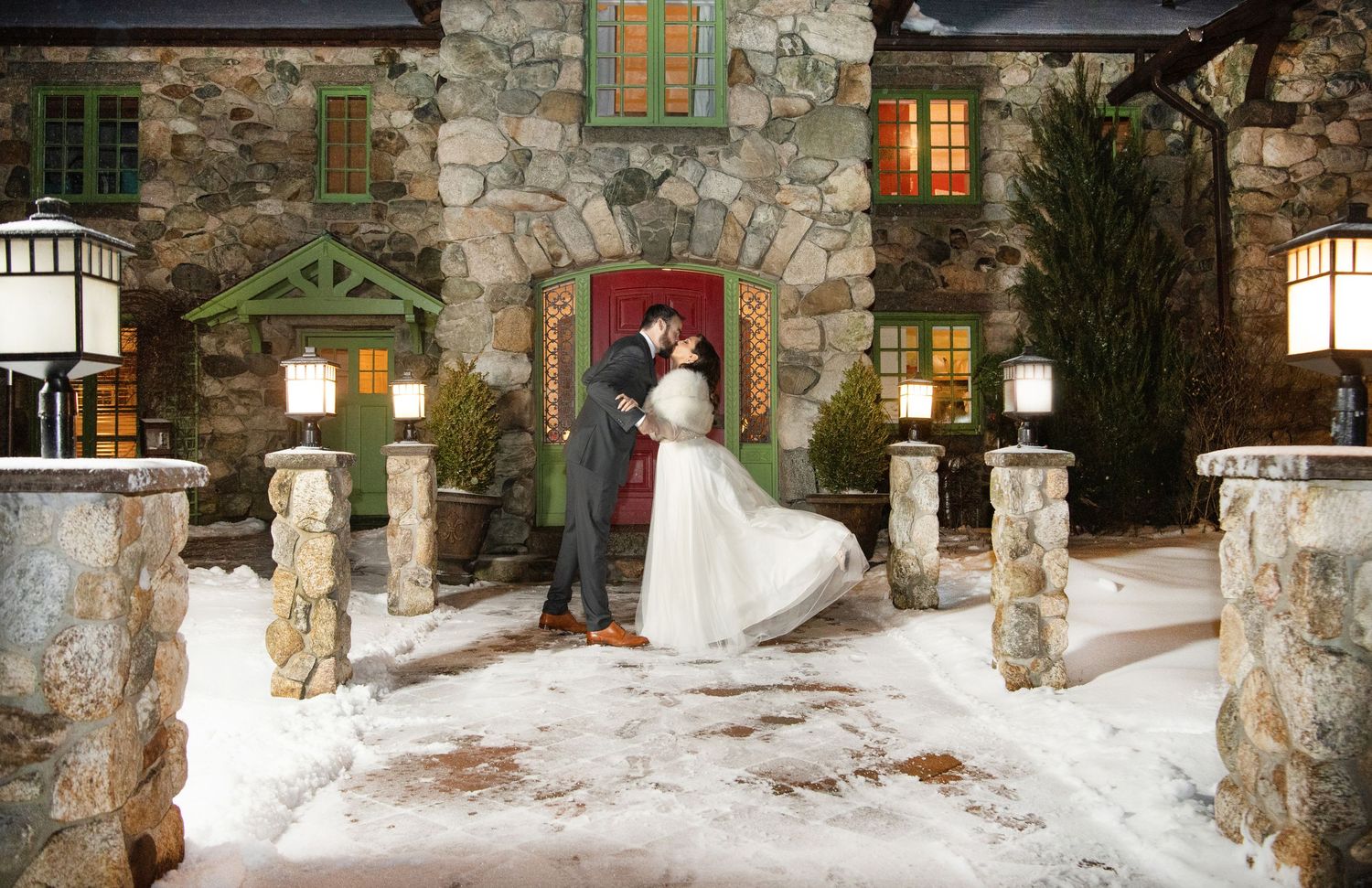 Snow-covered stone pathway lined with lanterns and winter decorations at a rustic wedding venue.