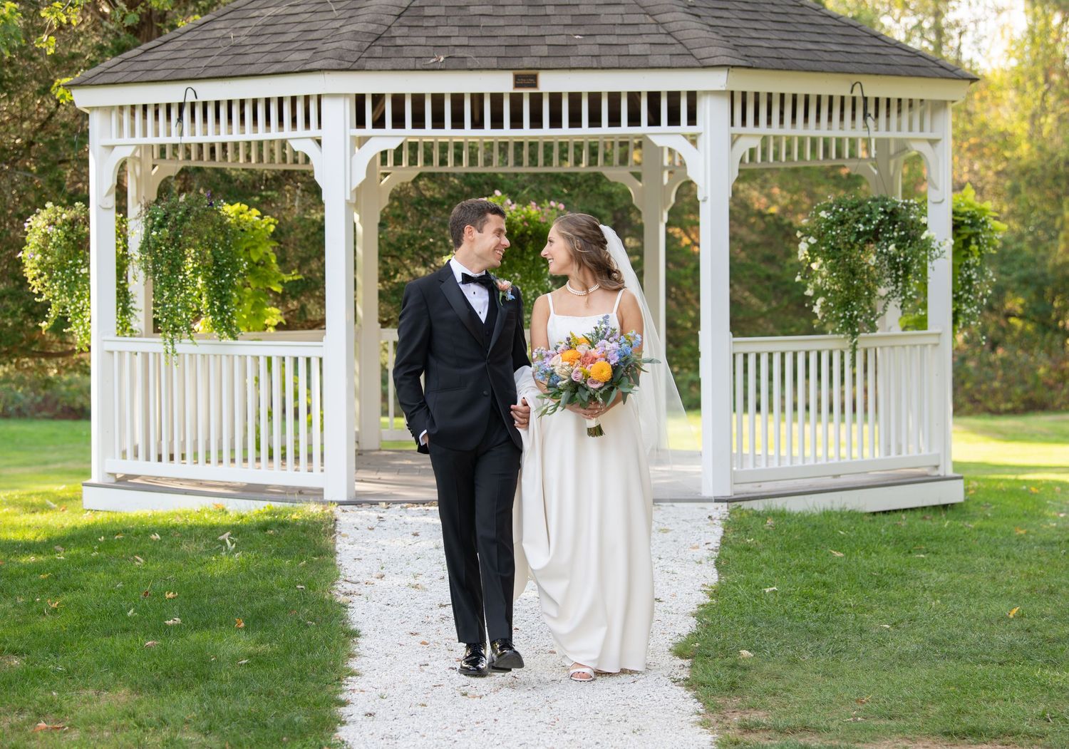 Romantic couple shares tender moments near white gazebo in lush garden setting during golden hour.