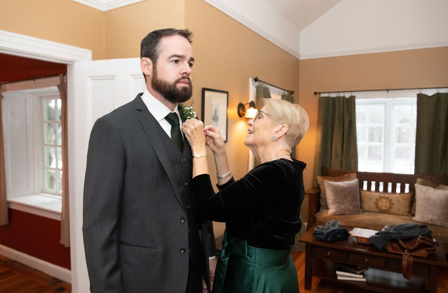 A couple getting ready for a formal event, with one person adjusting the other's tie in a warmly lit room.