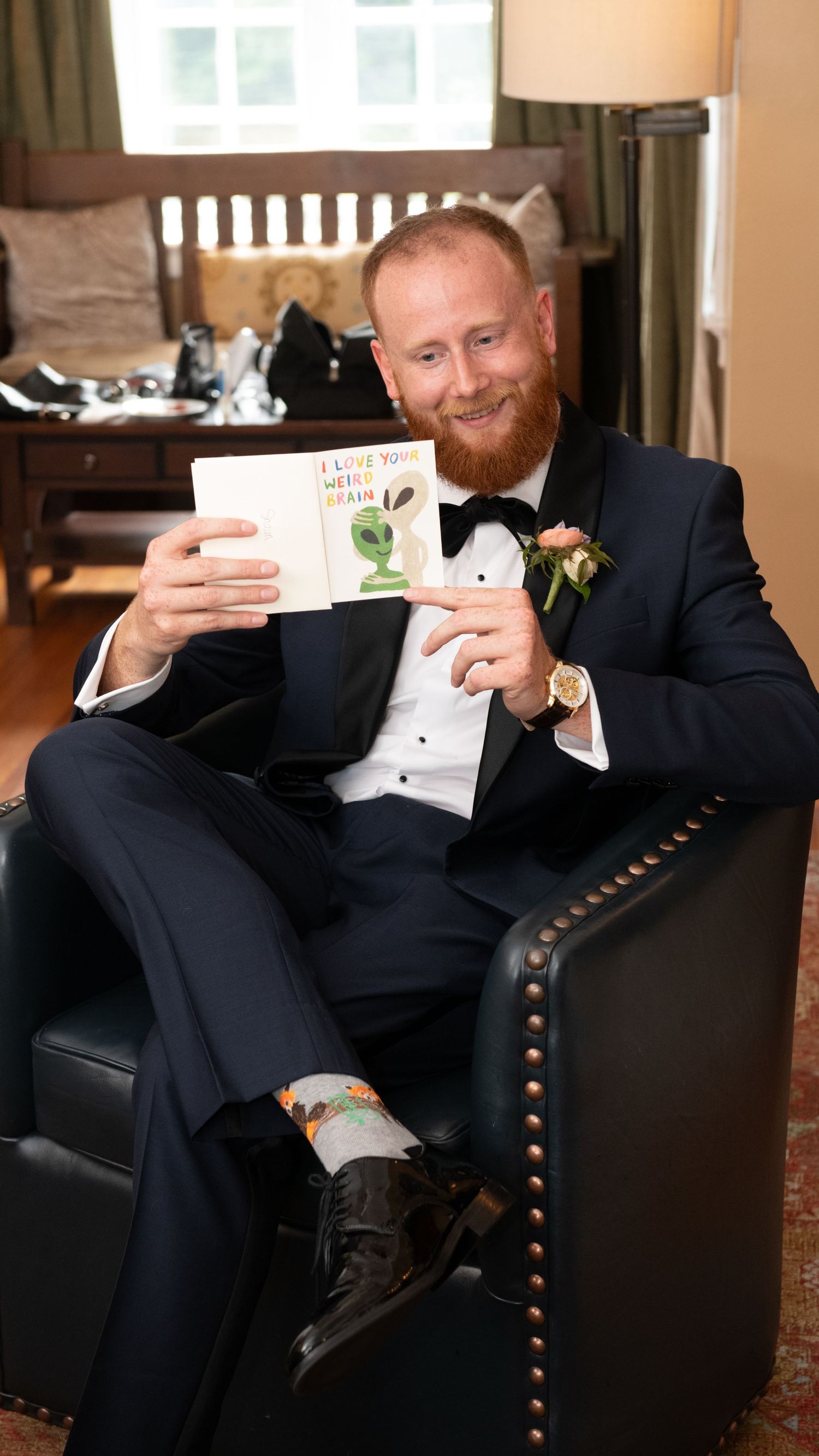 A person in a black tuxedo relaxes in an upholstered armchair during a formal event.