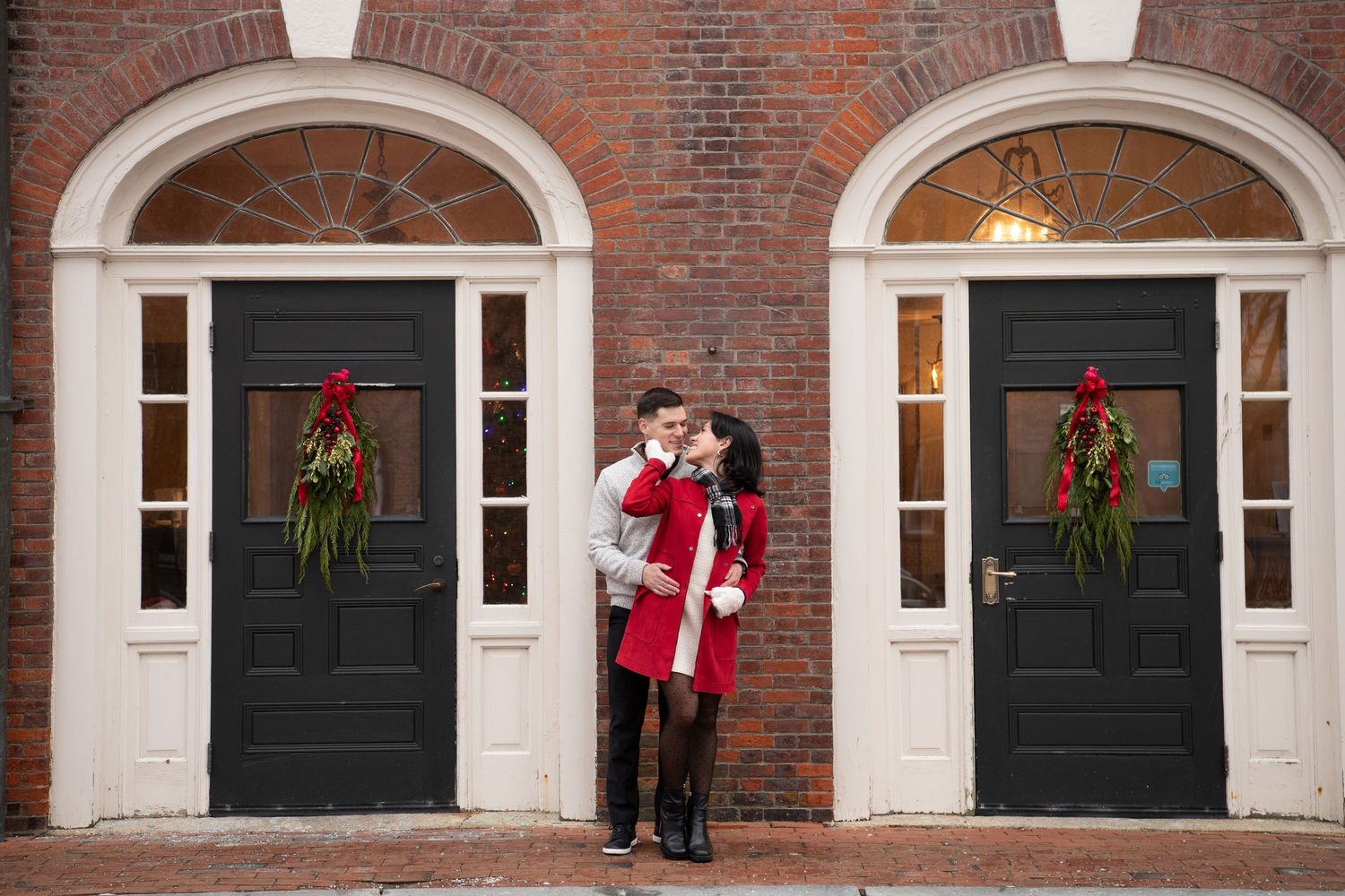 A sequence of photos showing a couple in winter attire posing in front of a classic brick building with black doors and wreaths.