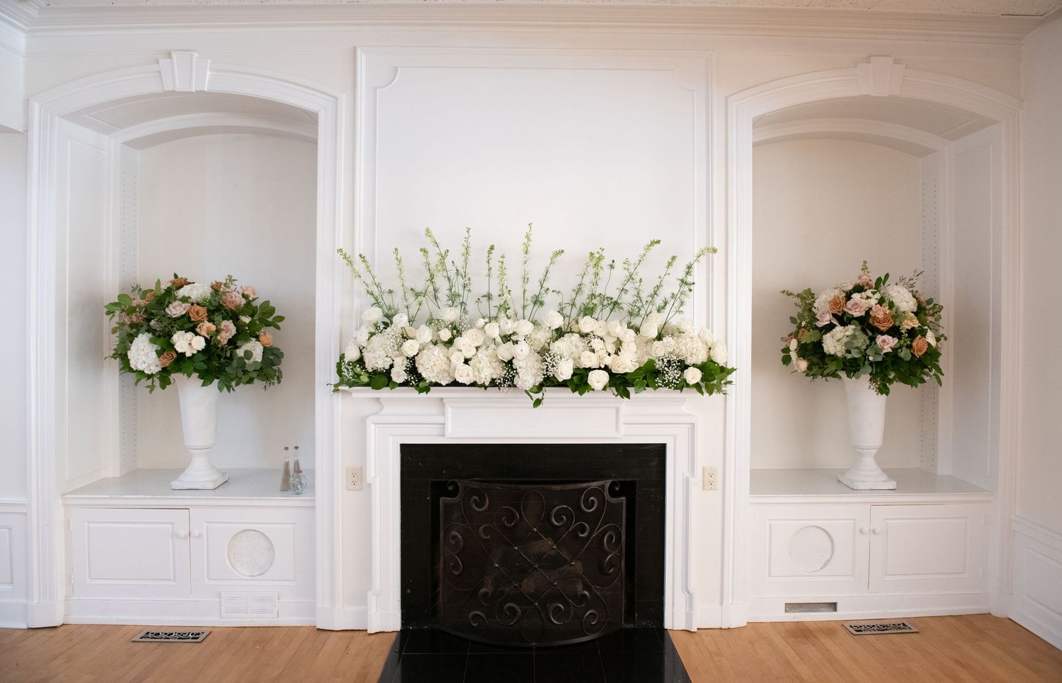 Elegant white wedding ceremony space with ornate moldings and floral arrangements decorating the front.
