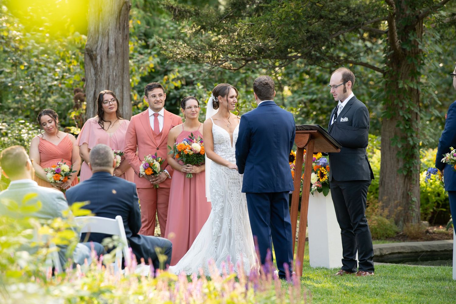 Outdoor wedding ceremony in a garden setting with yellow wildflowers and trees in the background.