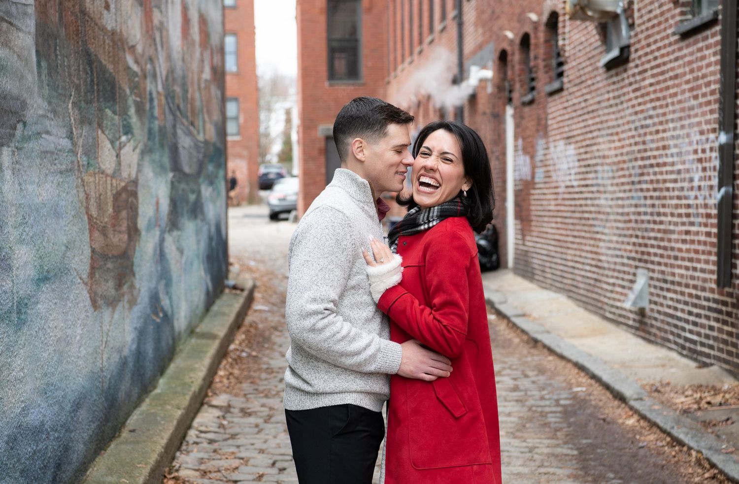 A couple embraces in a romantic moment along a brick-lined alley in an urban setting.