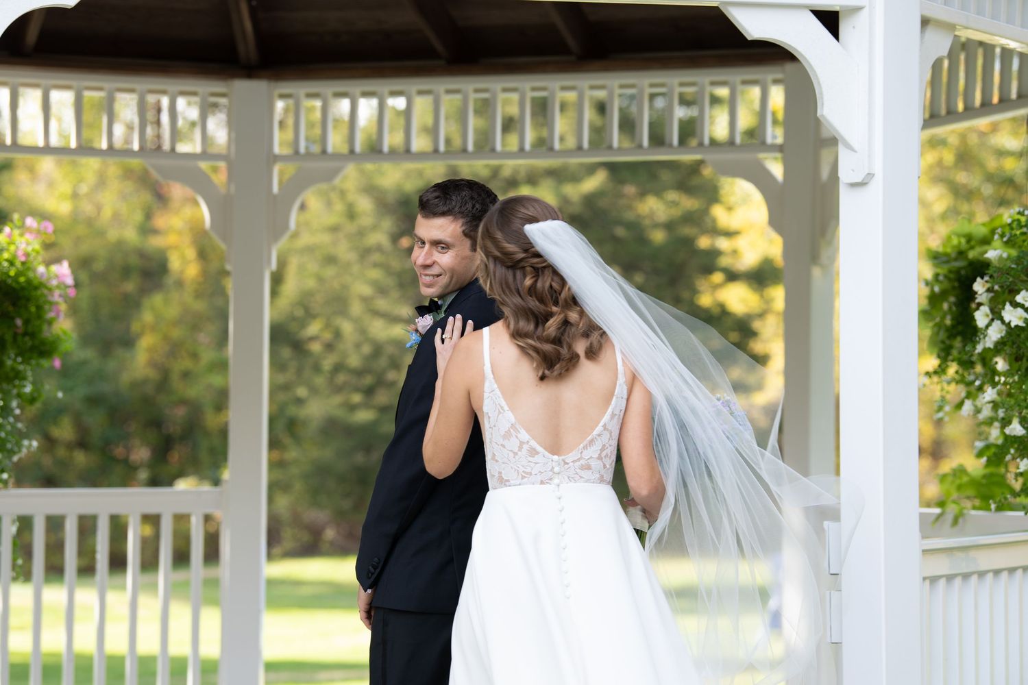 A couple poses together under a white gazebo in a romantic garden setting.