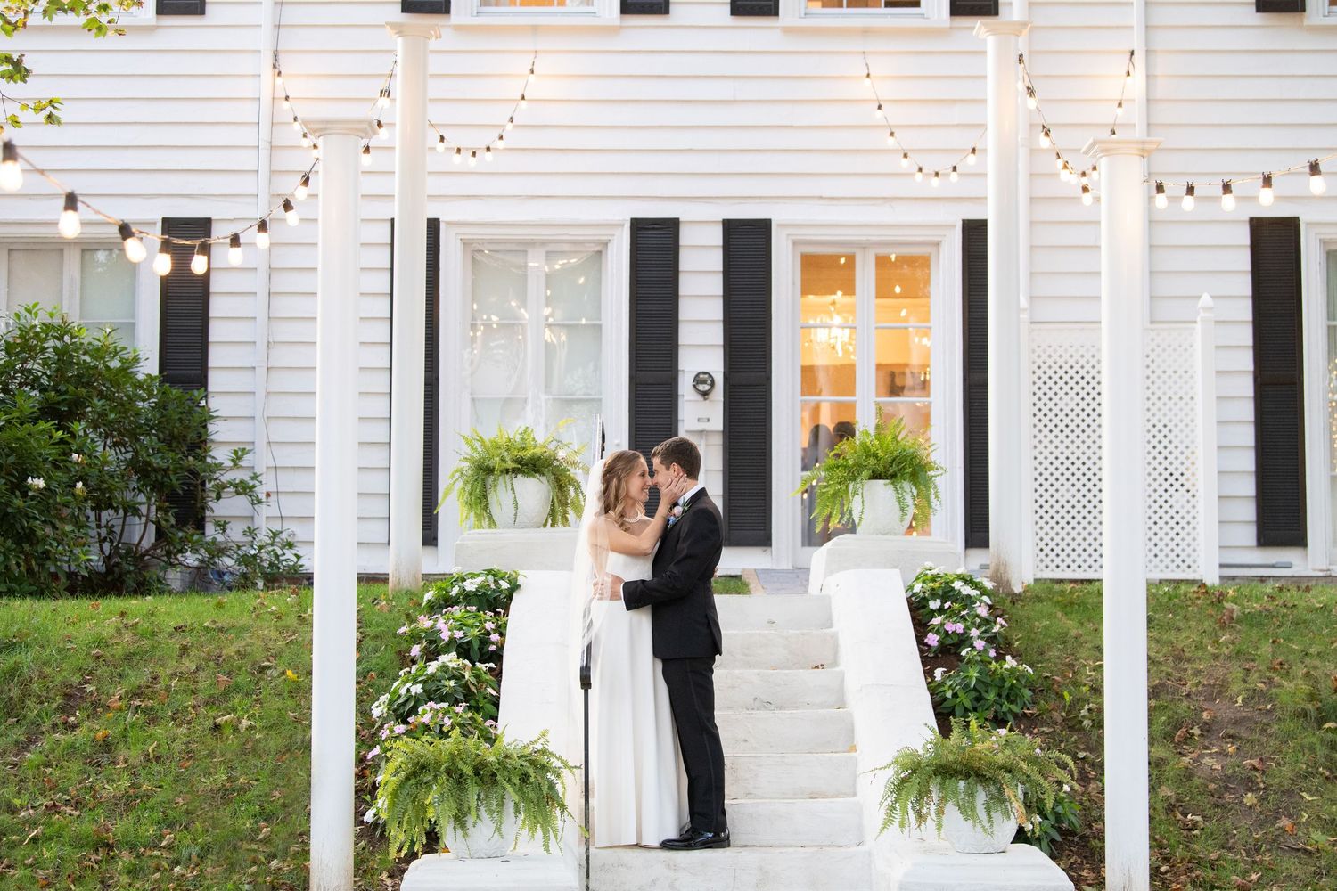 White pergola decorated with string lights creates a romantic outdoor setting with hanging ferns and potted plants.
