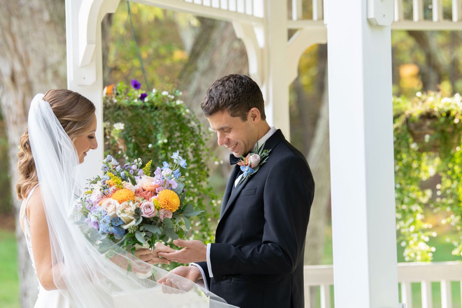 A romantic couple shares tender moments during their outdoor wedding ceremony under a white gazebo.